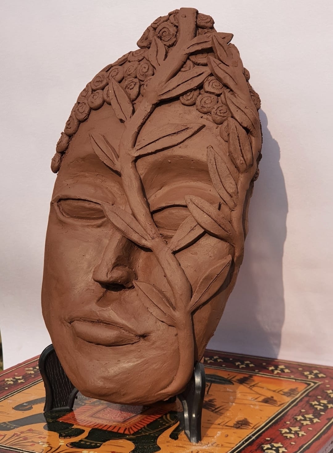 Terracotta face sculpture with leaves and flowers across it
